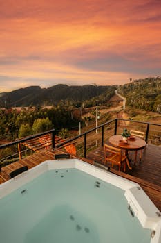 Relax on a luxury patio with a hot tub overlooking a scenic rural landscape at sunset.